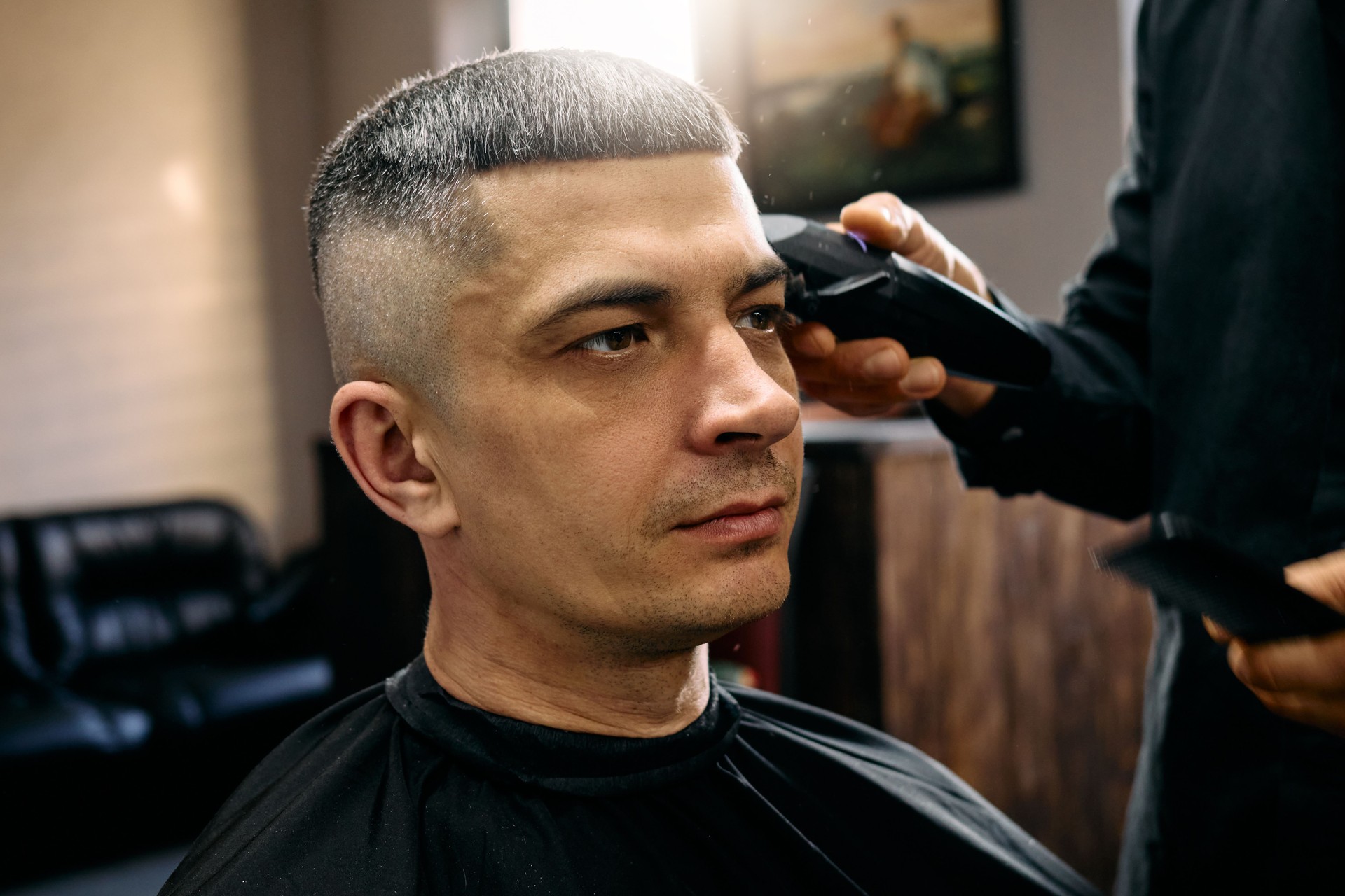 A skilled hairdresser is giving a man a fresh haircut in a contemporary barbershop. The atmosphere is relaxed, with natural light illuminating the space